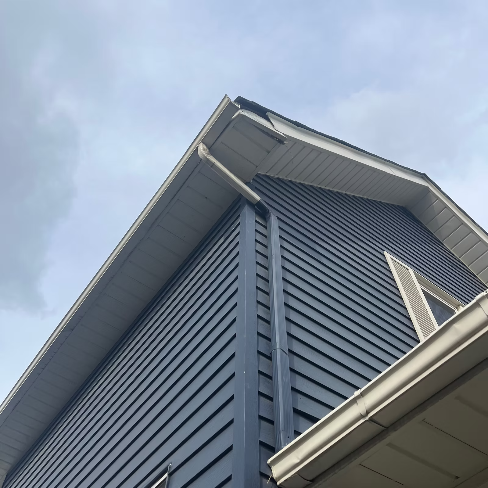 Dark blue siding on a building's corner with gray trim and gutters, against a cloudy sky.