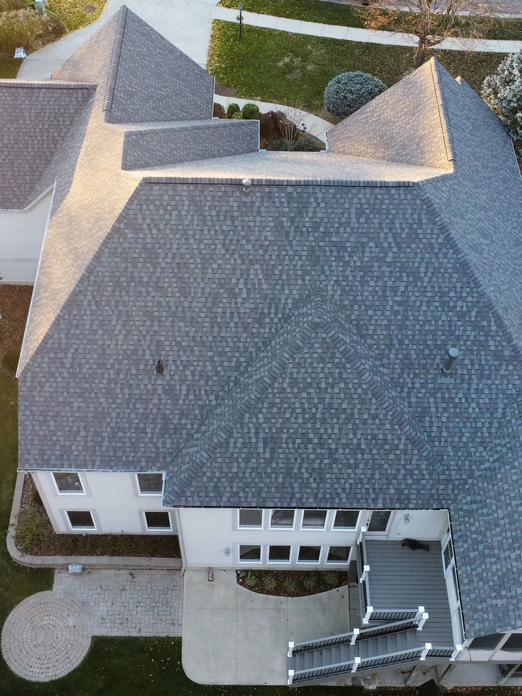 Aerial view of a gray shingled roof on a white house with a patio and deck.