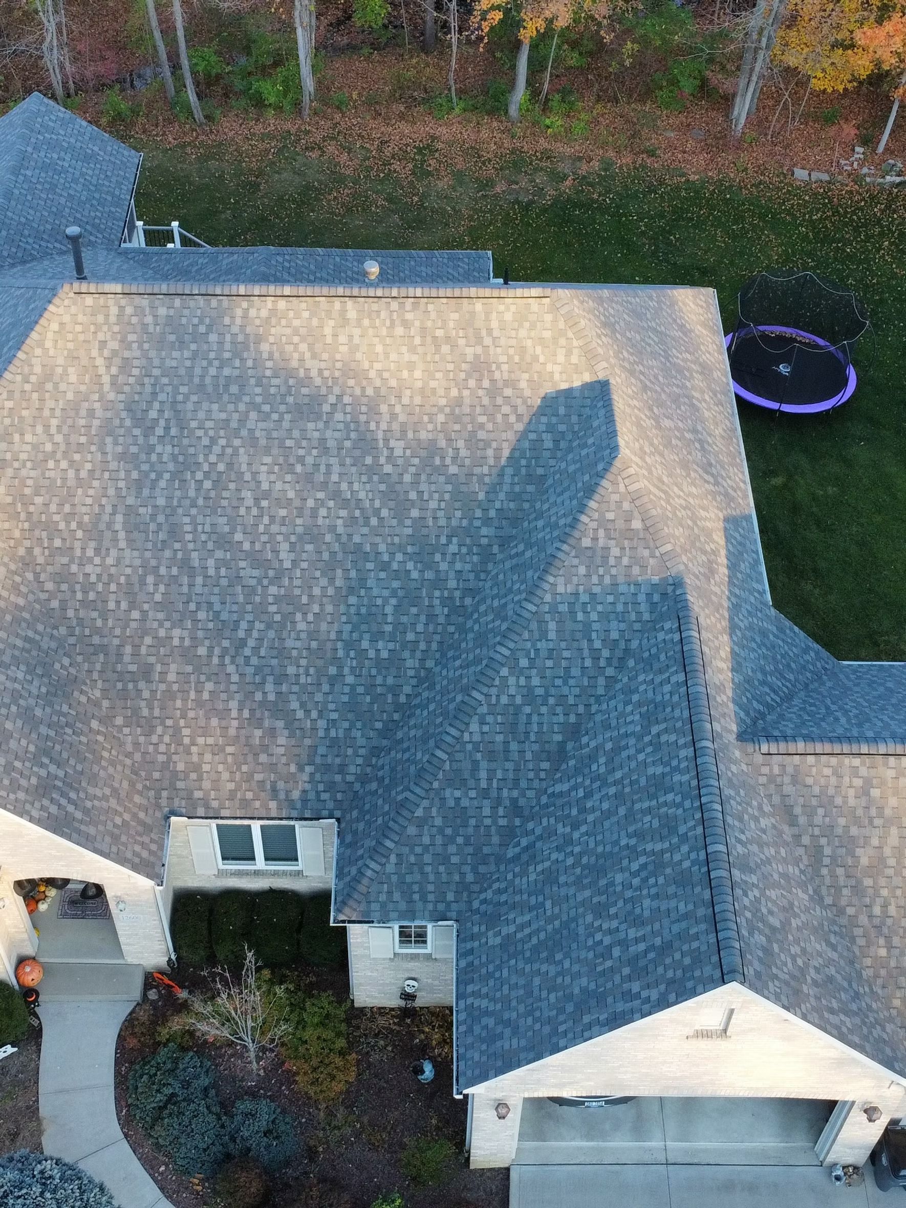 Overhead view of a house with a gray shingled roof, lawn, trees and a trampoline.