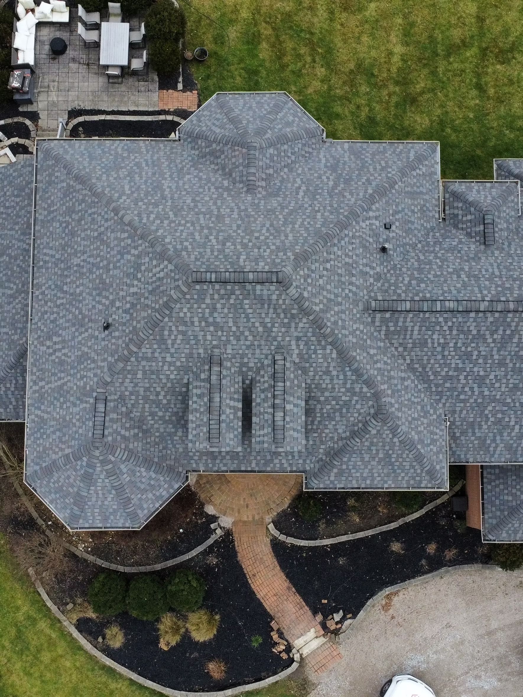 Aerial view of a gray asphalt shingle roof on a house, with a brick path leading to the entrance.