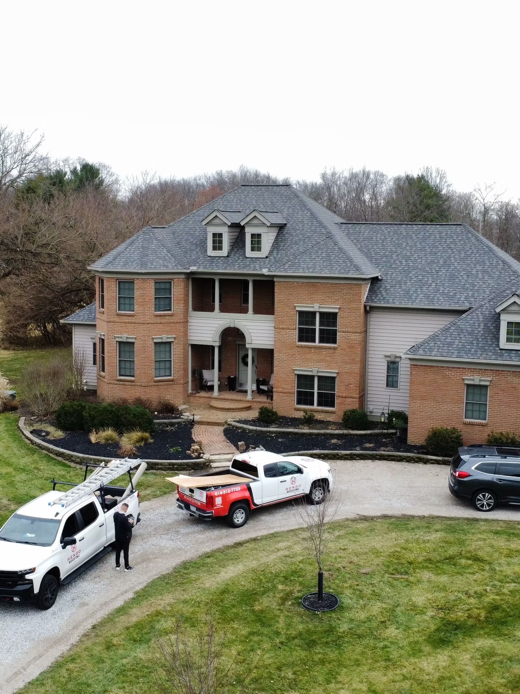 House with workers and trucks on the driveway; roofing or construction in progress.