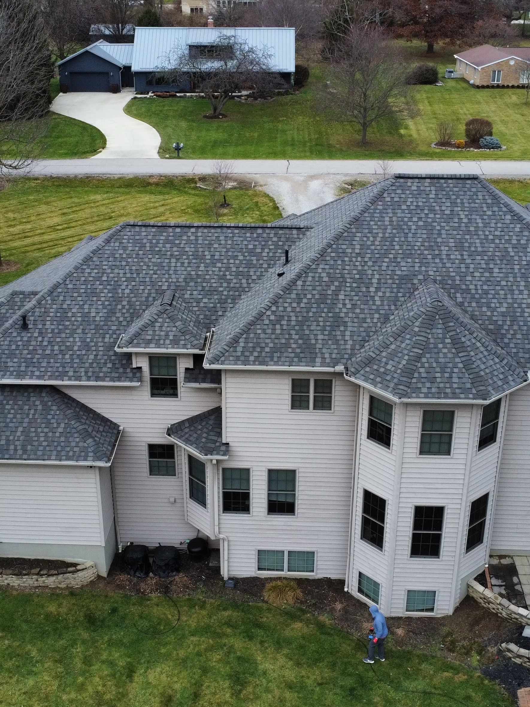 Overhead view of a large house with a gray roof and white siding; a person is in the yard.