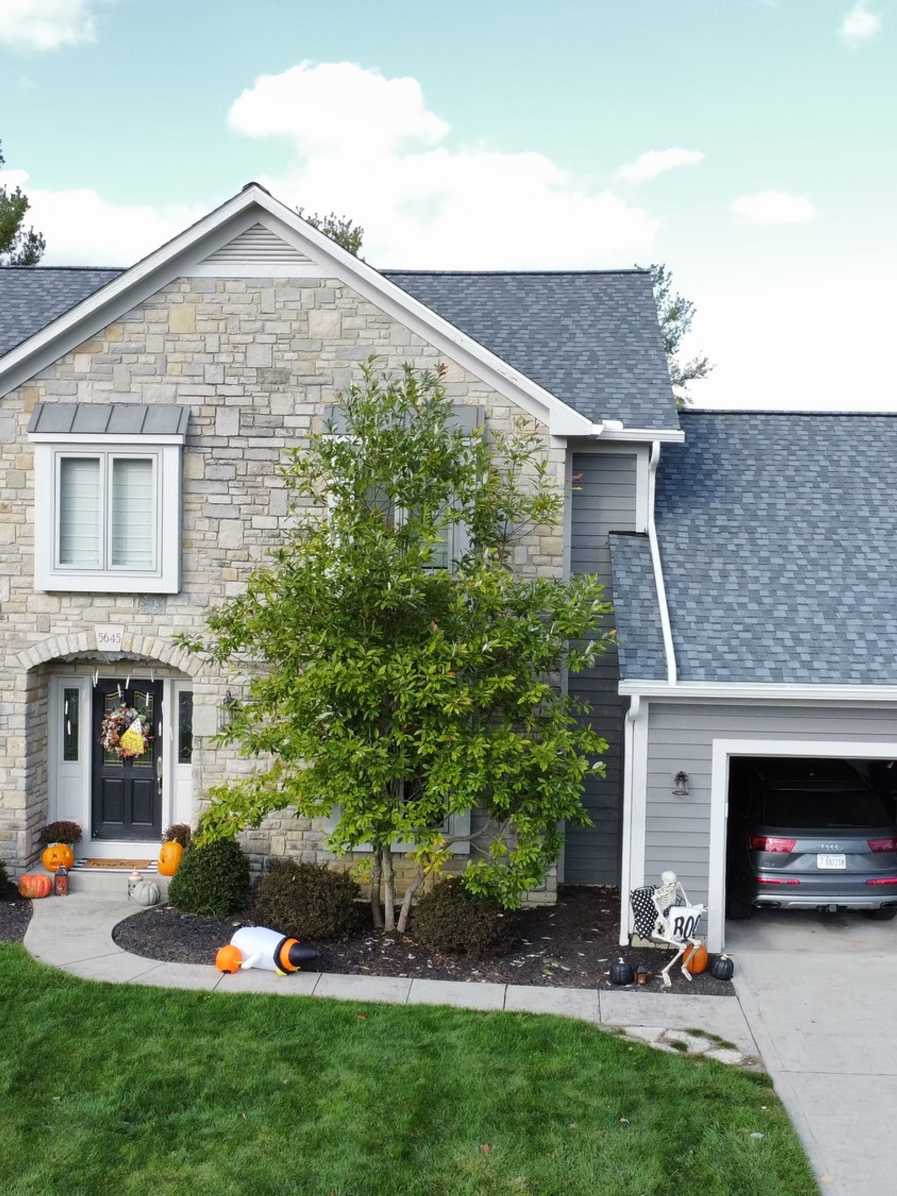 House with stone facade, gray roof, decorated for Halloween with pumpkins and a wreath.