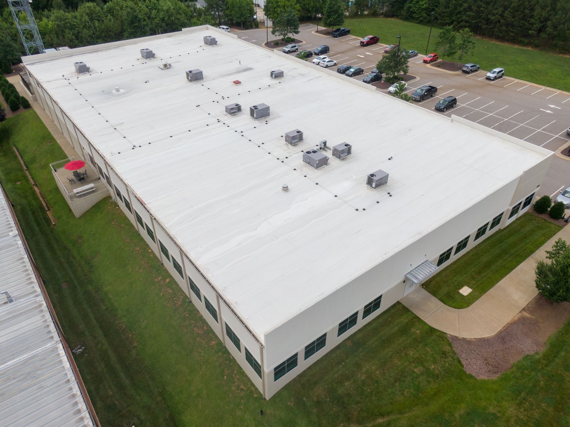 Large commercial building with a white roof, air conditioning units, and a parking lot.
