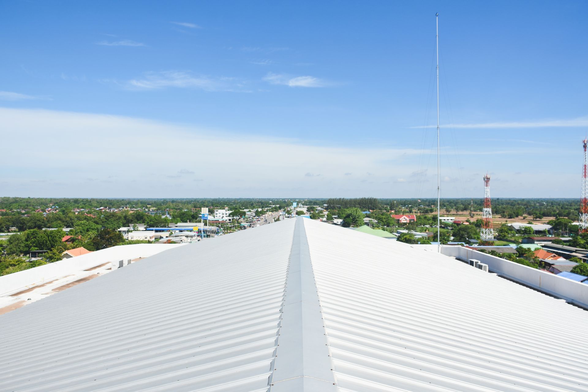 Wide view of a long, corrugated metal roof with a town and blue sky in the background.