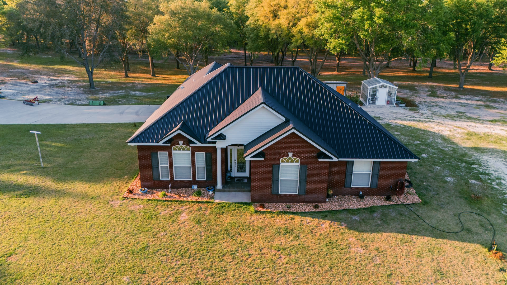 Brick house with a dark roof and white trim, surrounded by grass and trees.