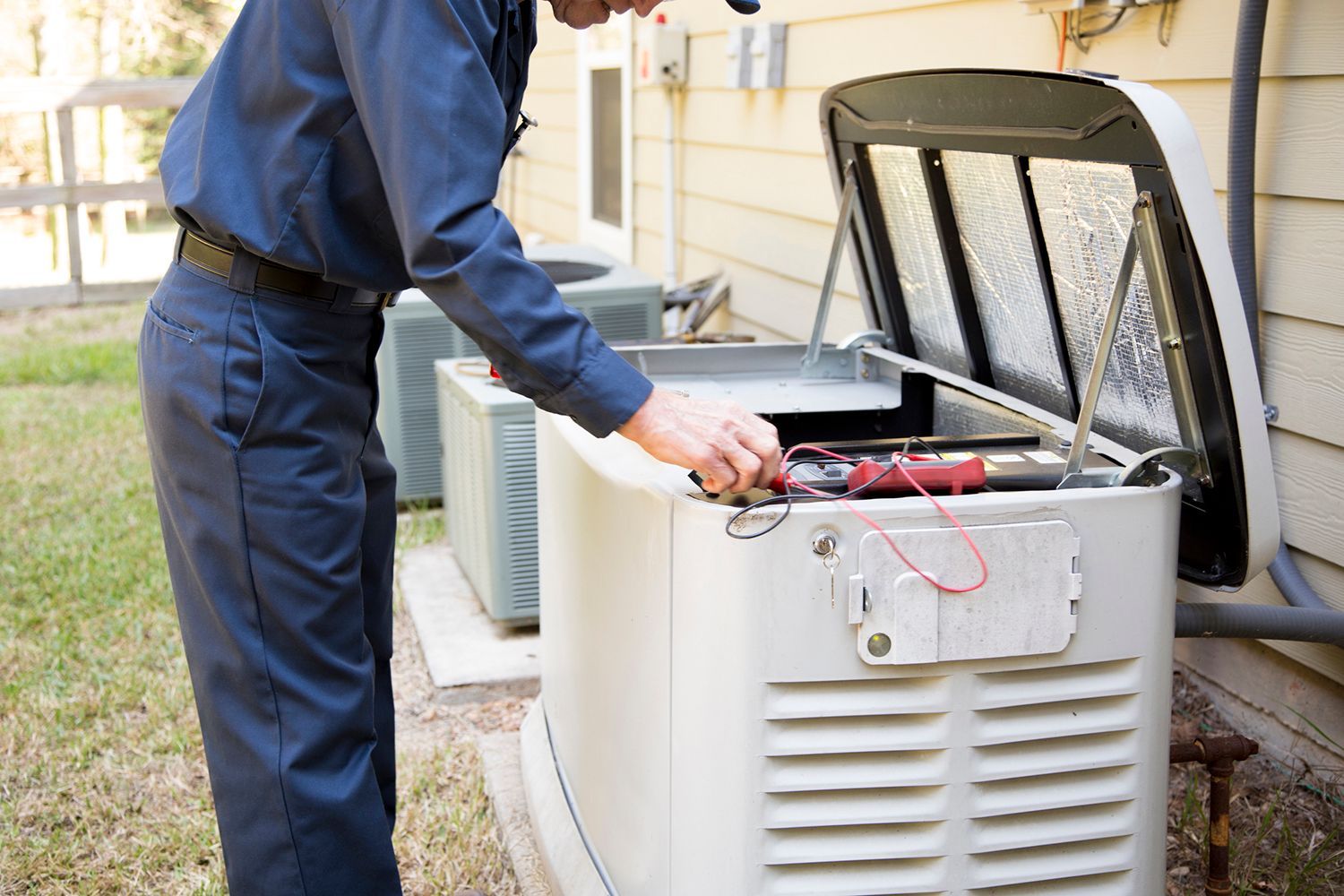 Technician in blue overalls, working on a generator outside a house.
