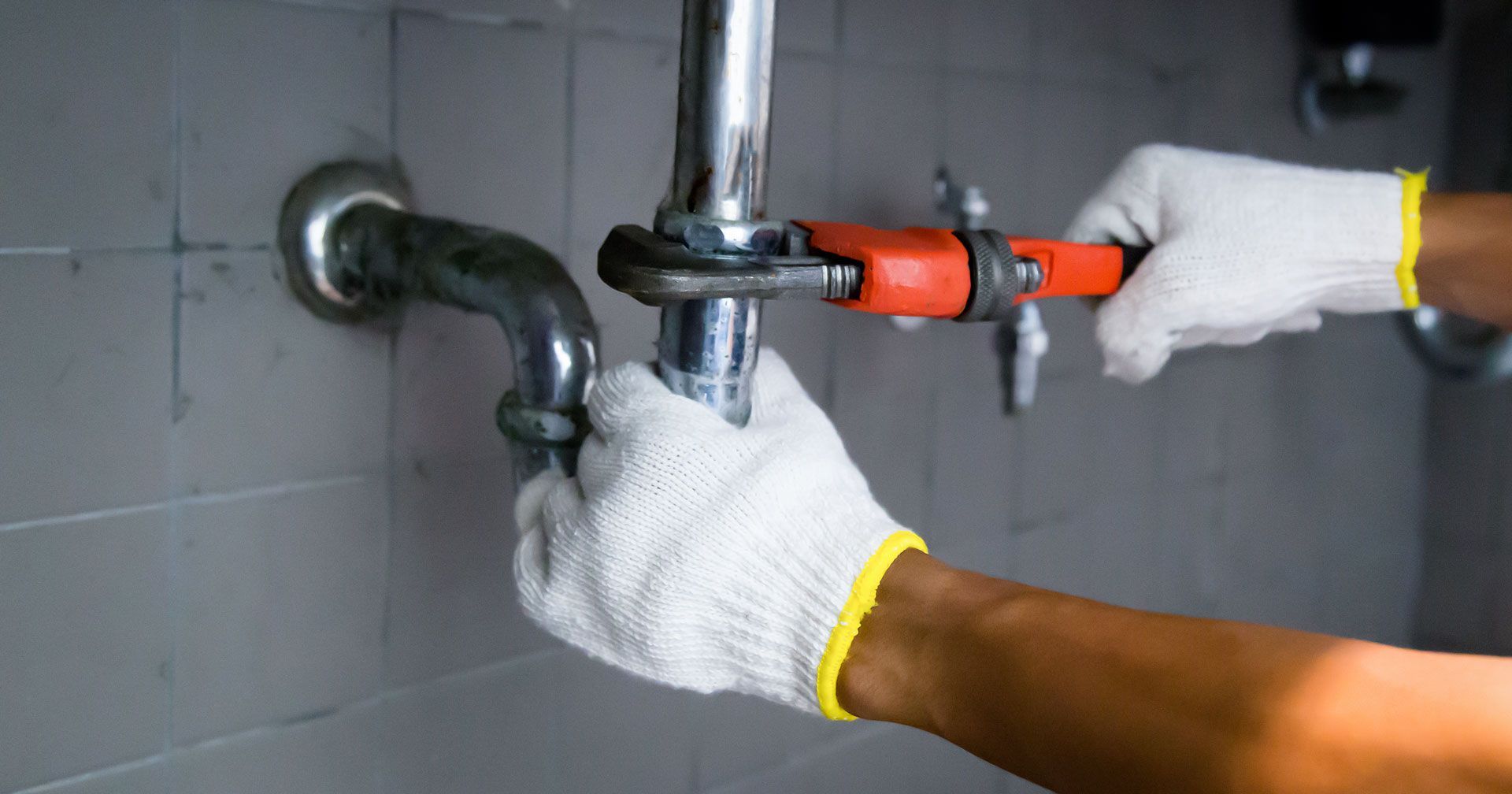 Plumber with a wrench fixing a pipe in a bathroom, wearing gloves.