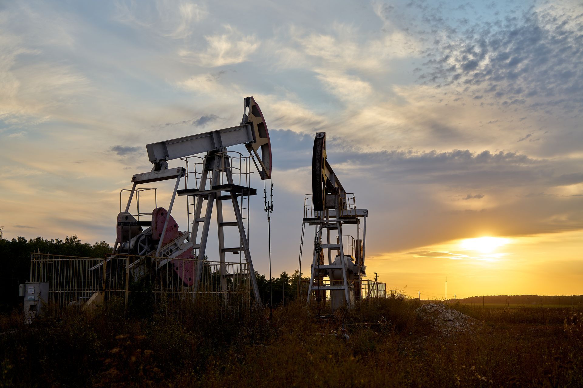 Two oil pumps in a field at sunset.