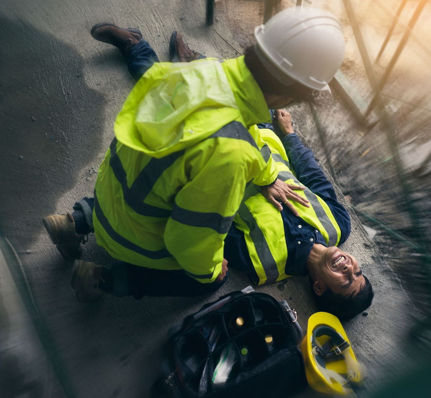 A man in a hard hat is helping a construction worker who is laying on the ground.