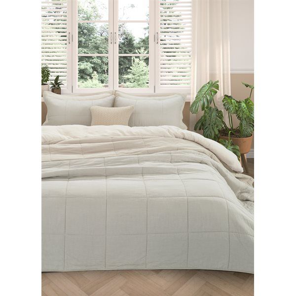 A bed with a light-colored comforter, pillows, and a blanket