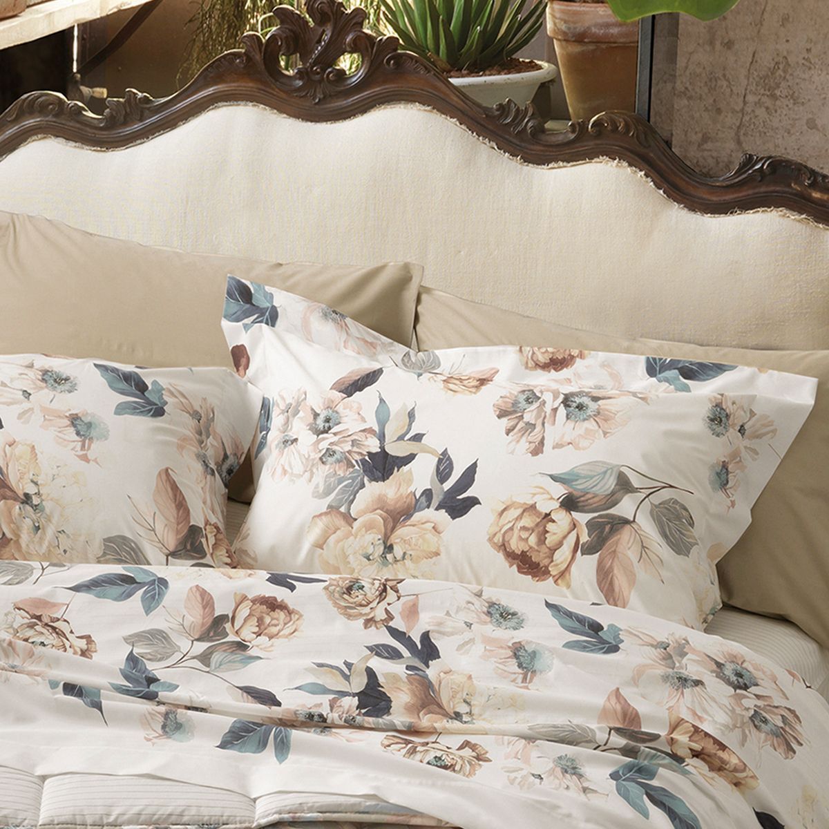 A bed with an ornate wooden headboard features pillows and bedding with floral print in tan and blue