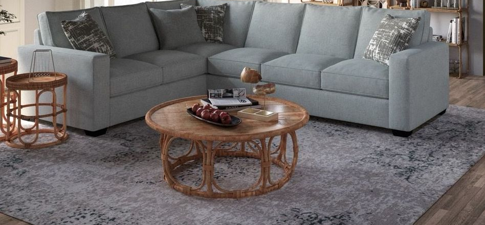 Gray sectional sofa in a bright living room with a glass coffee table, rug, and shelving unit