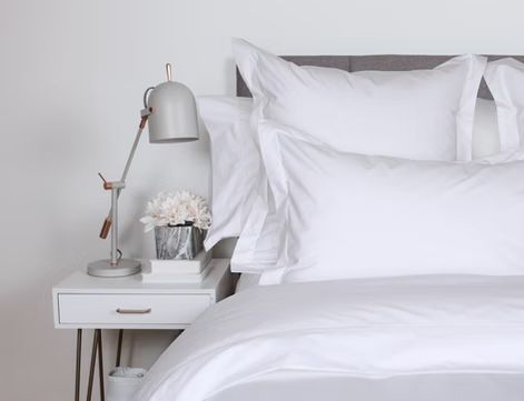 White bedding on a bed with a nightstand, lamp, and floral arrangement