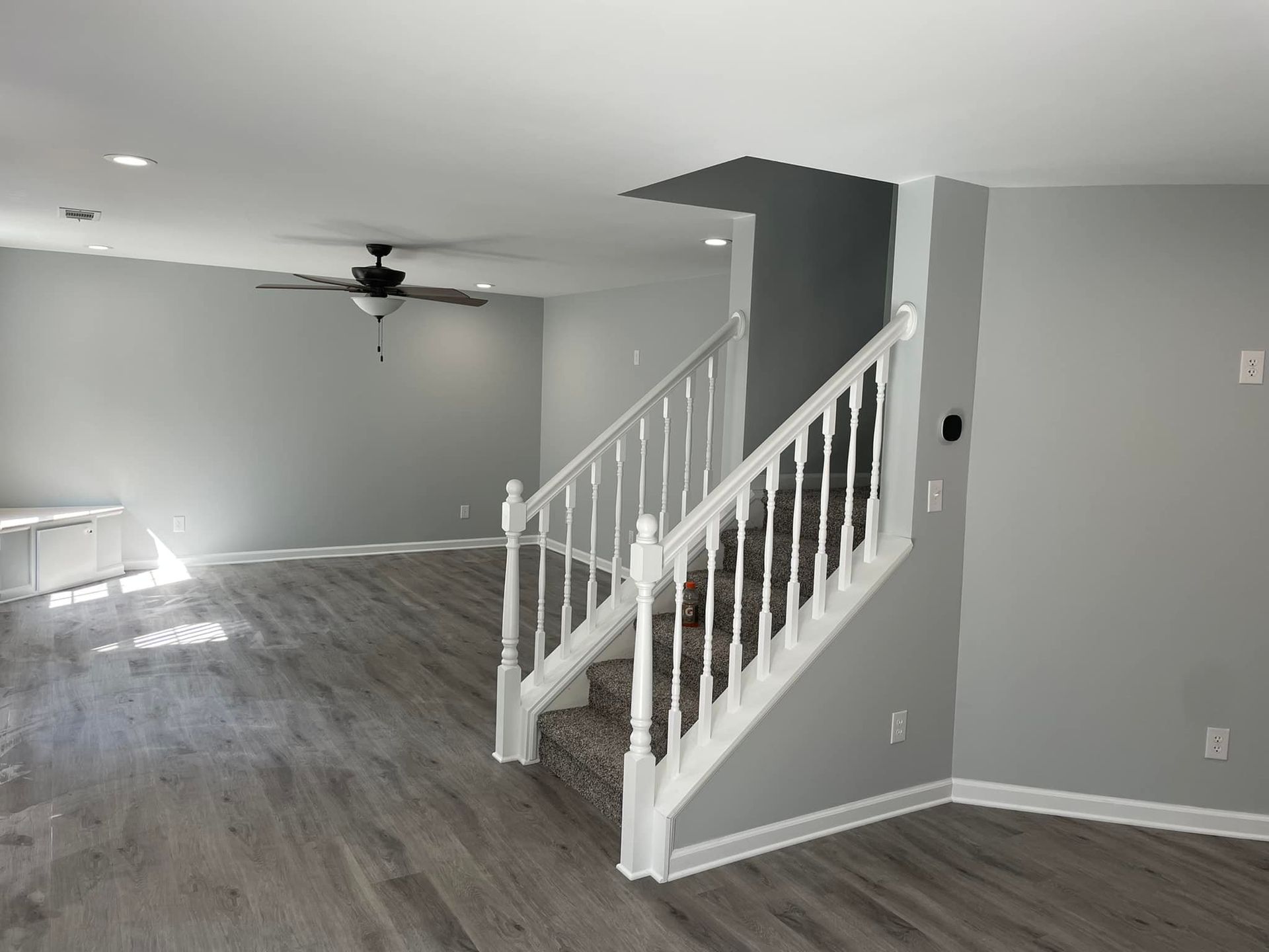 An empty living room with stairs and a ceiling fan.