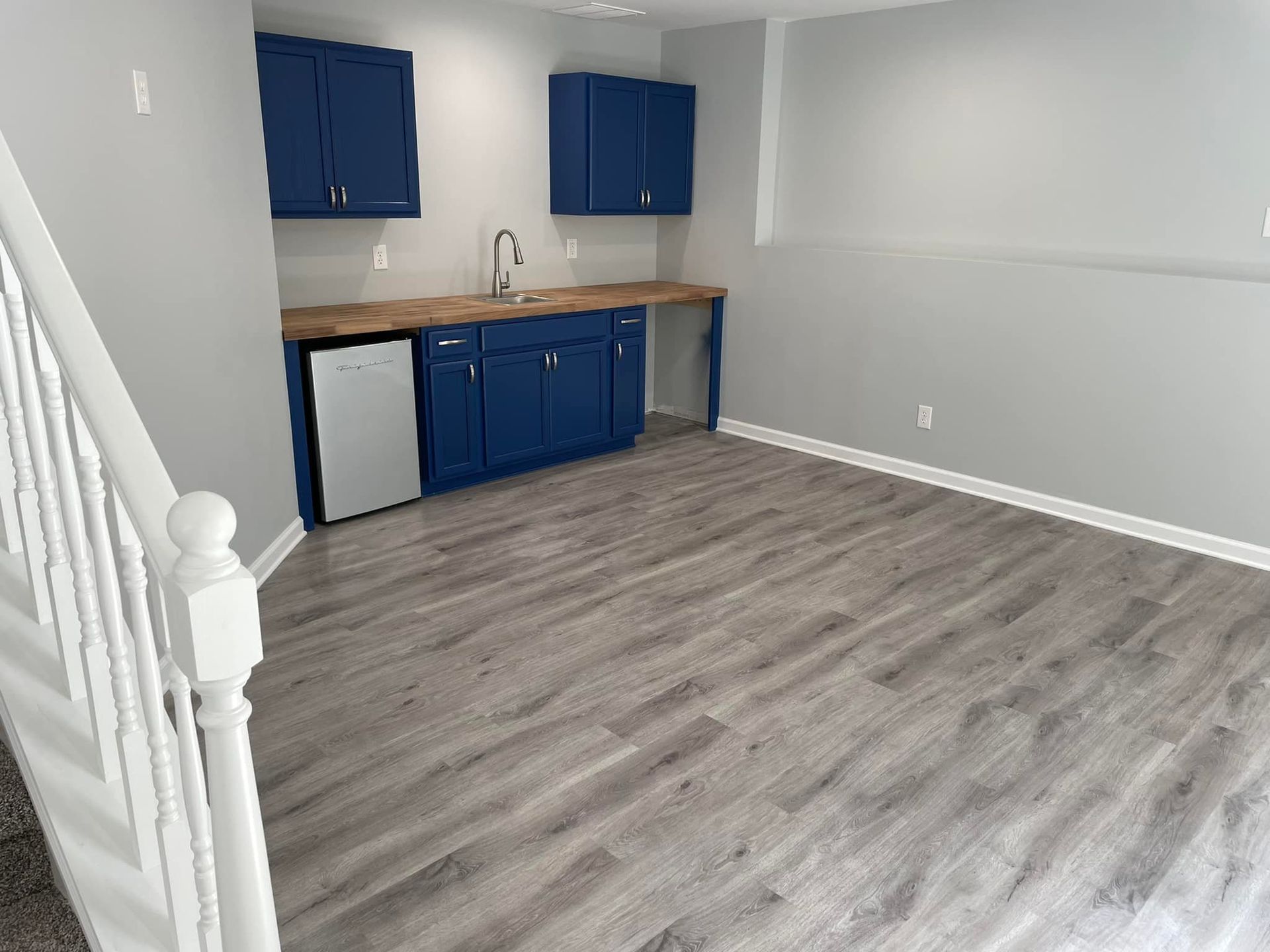 An empty basement with blue cabinets , a sink , and a dishwasher.