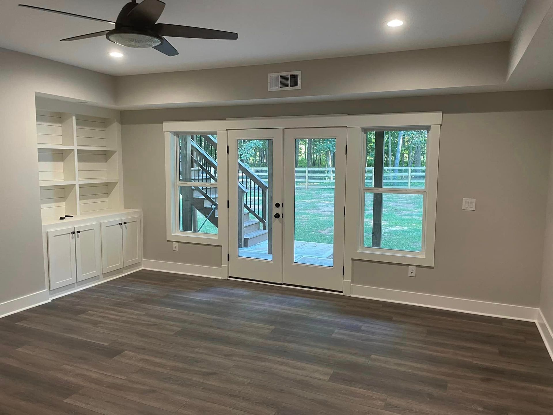 An empty living room with a ceiling fan and sliding glass doors.