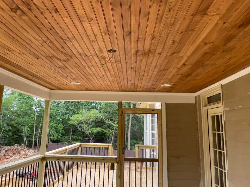 A screened in porch with a wooden ceiling and a wooden deck.