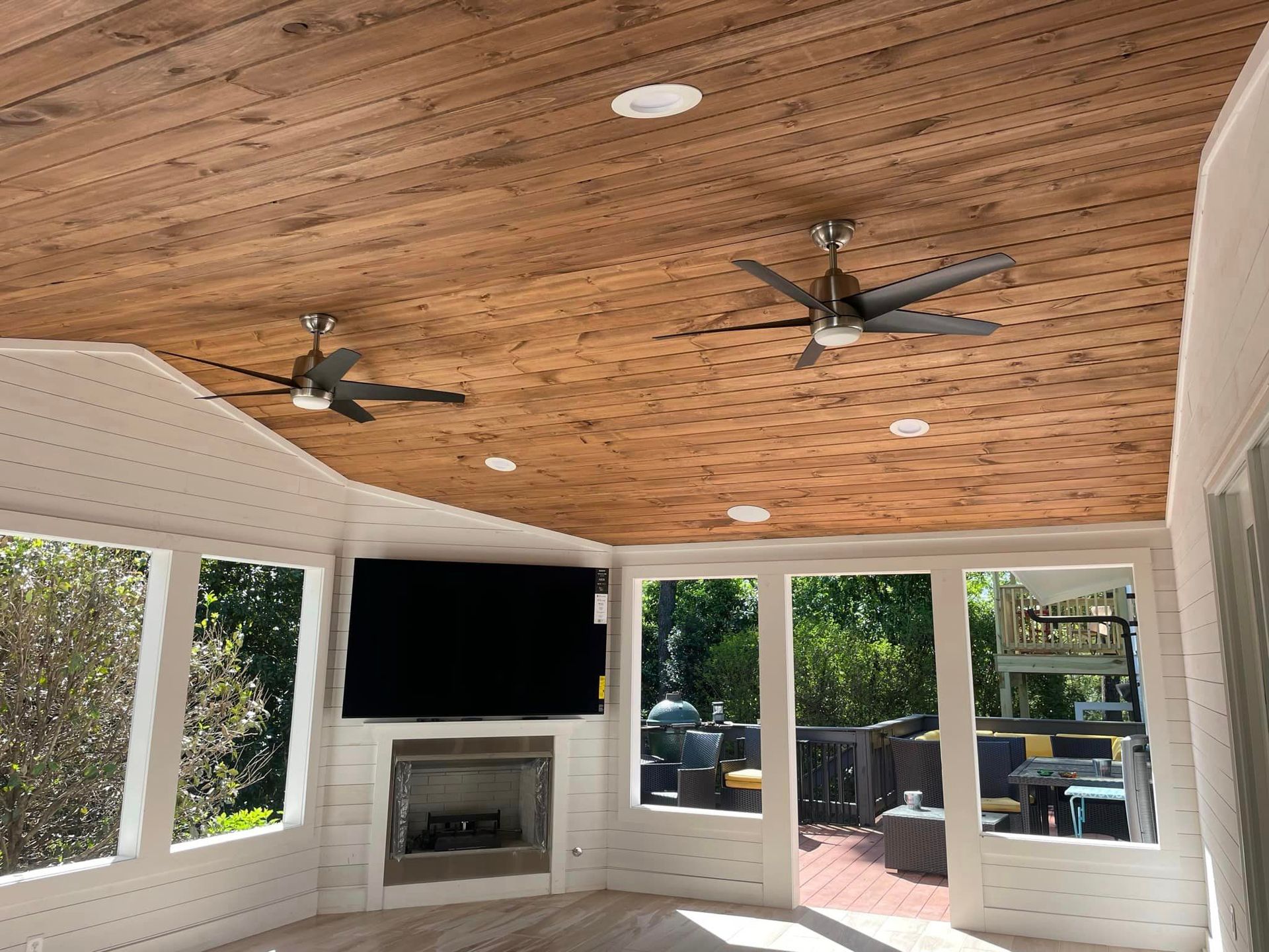 A screened in porch with a fireplace and ceiling fans