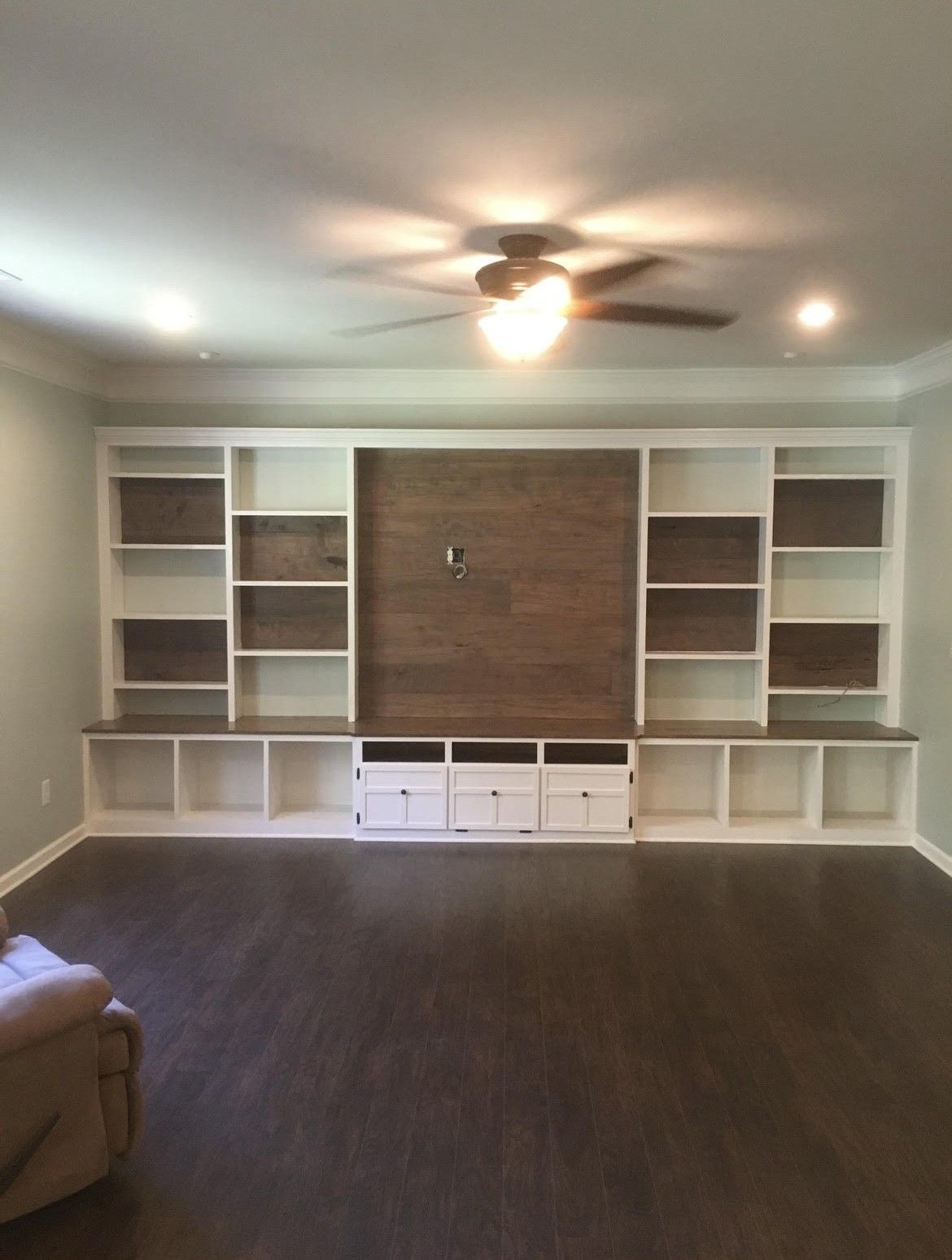 A living room with a large entertainment center and a ceiling fan.