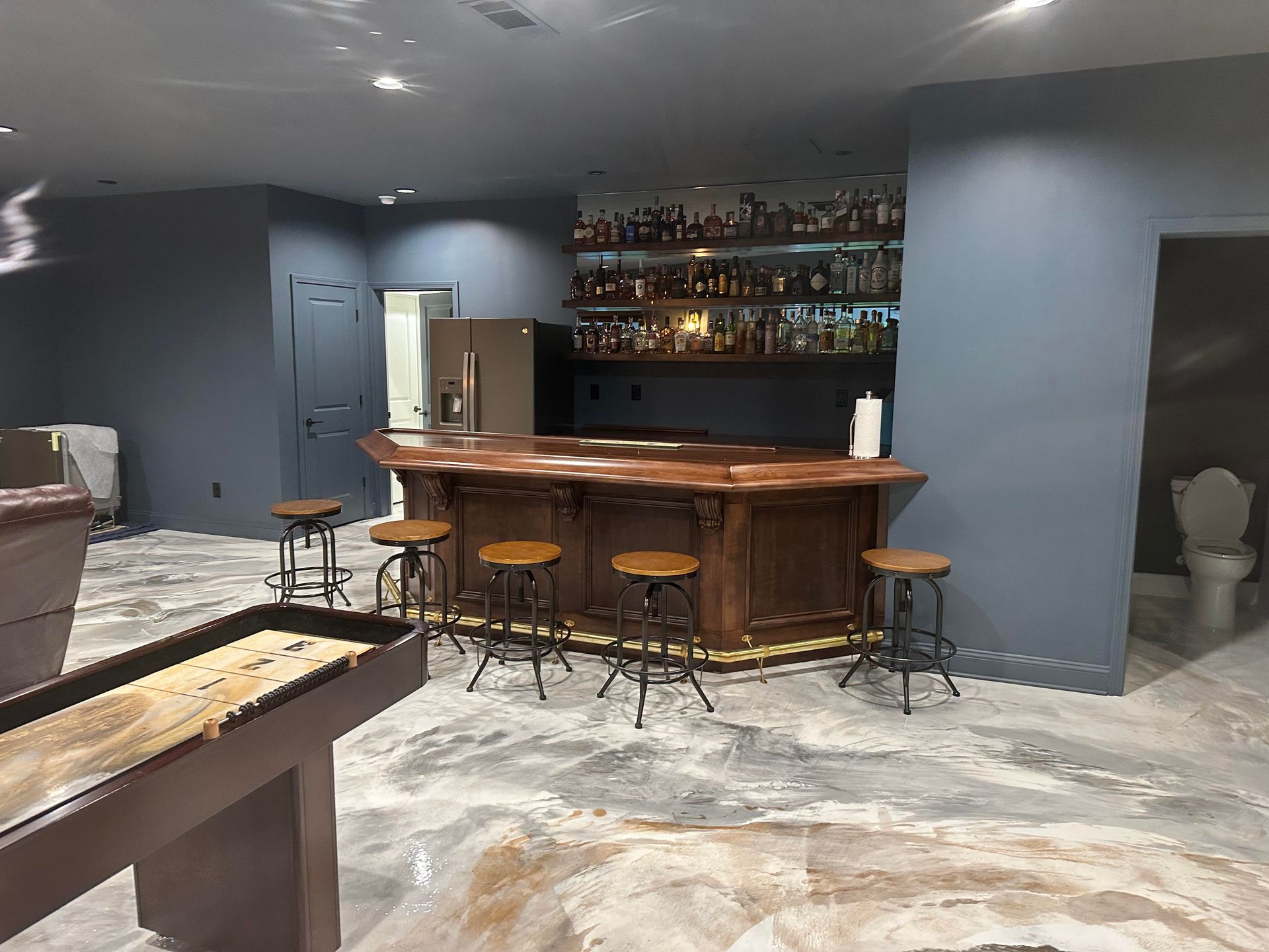 A basement with a bar , stools , a pool table and a toilet.