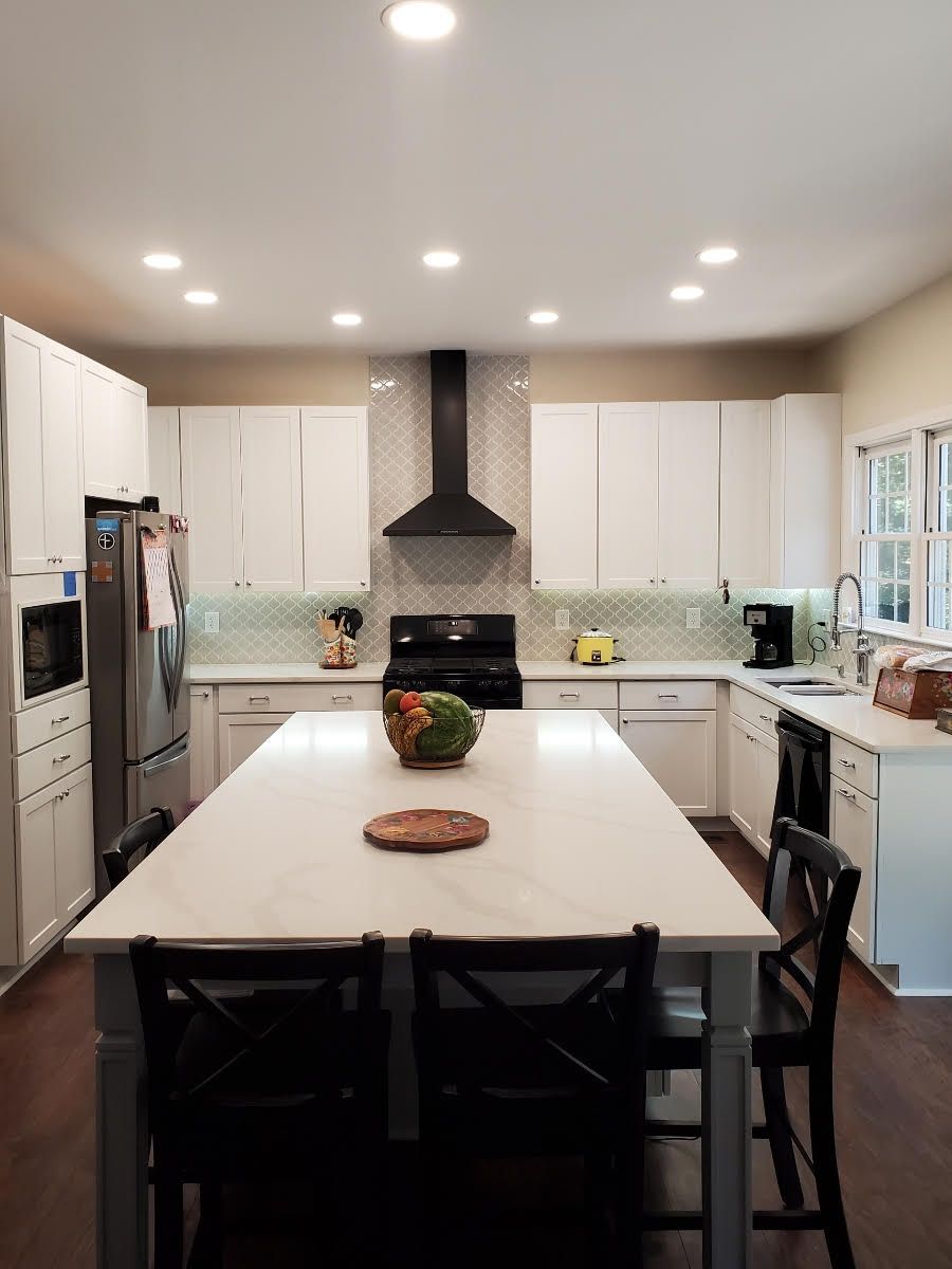 A kitchen with white cabinets , a large island , and stools.
