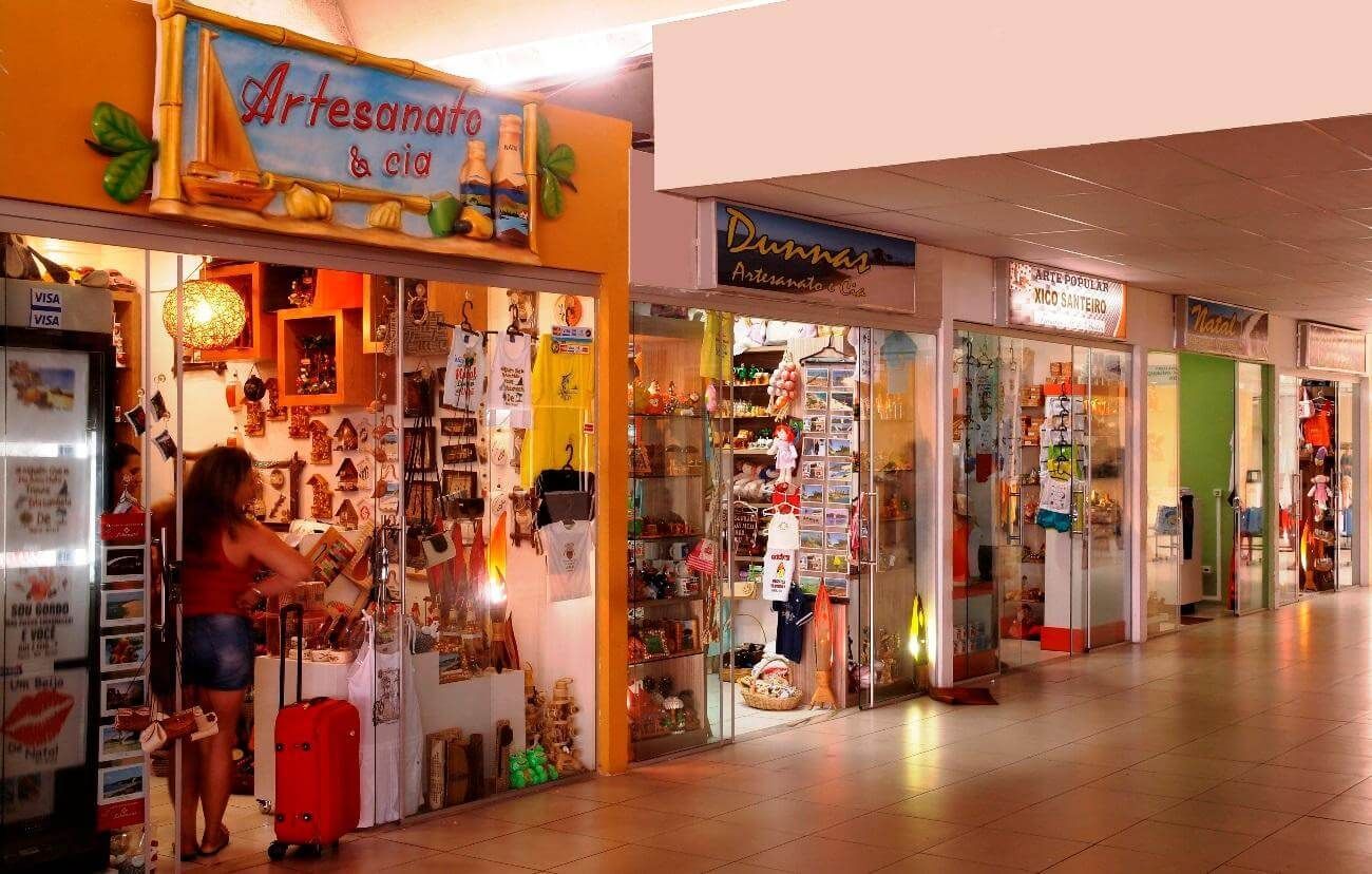 Galeria comercial interna com vitrines coloridas de lojas de artesanato e iluminação aconchegante ao longo de um corredor.