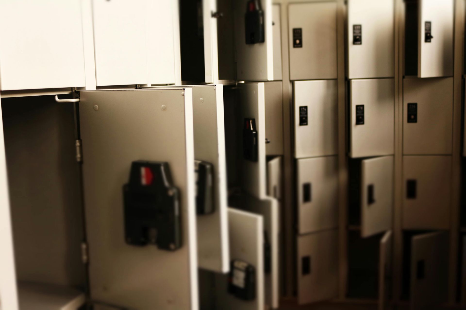 Fileiras de armários de metal branco, alguns abertos, em um ambiente com pouca luz