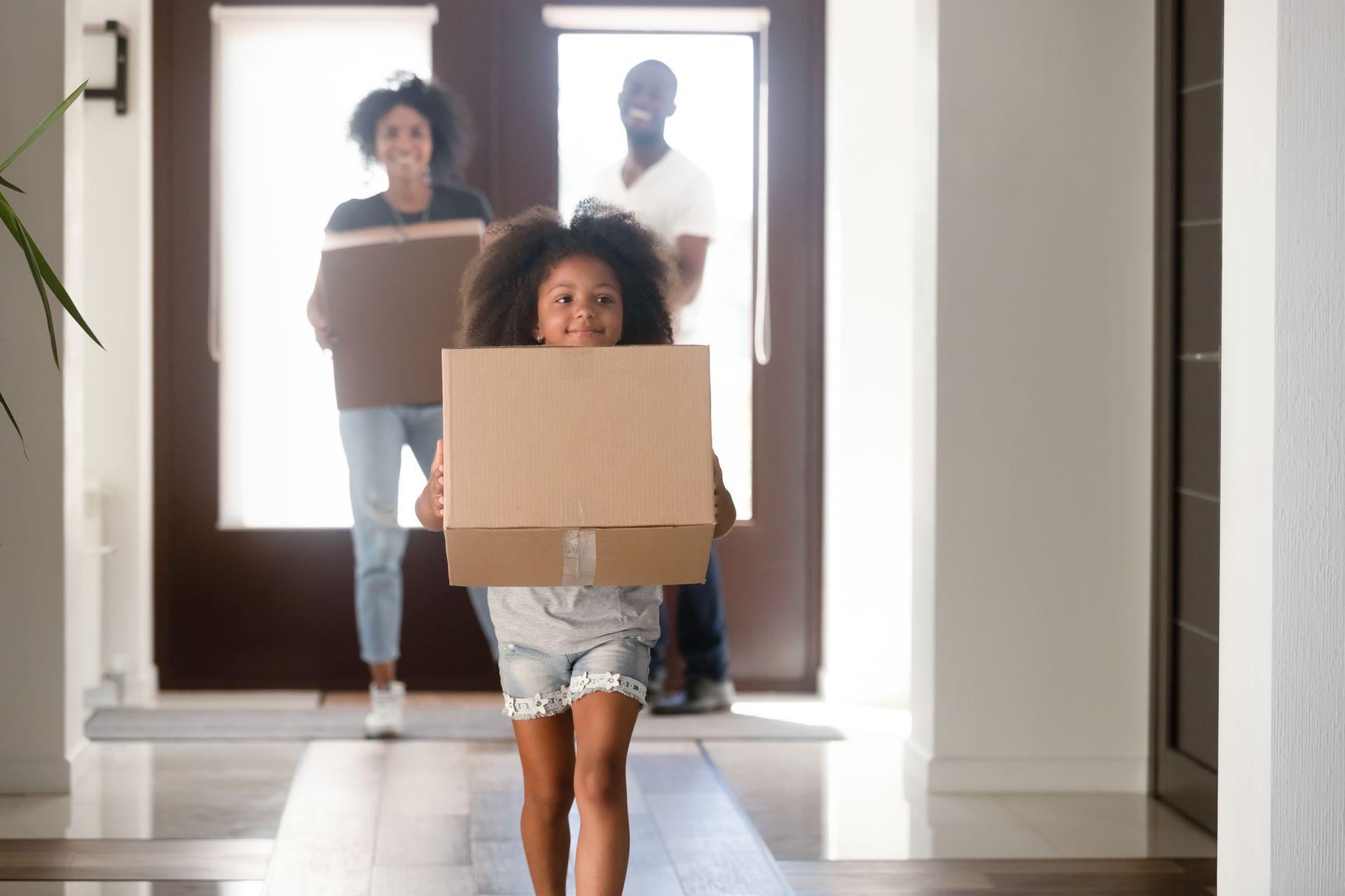 A little girl is carrying a cardboard box in front of a family.