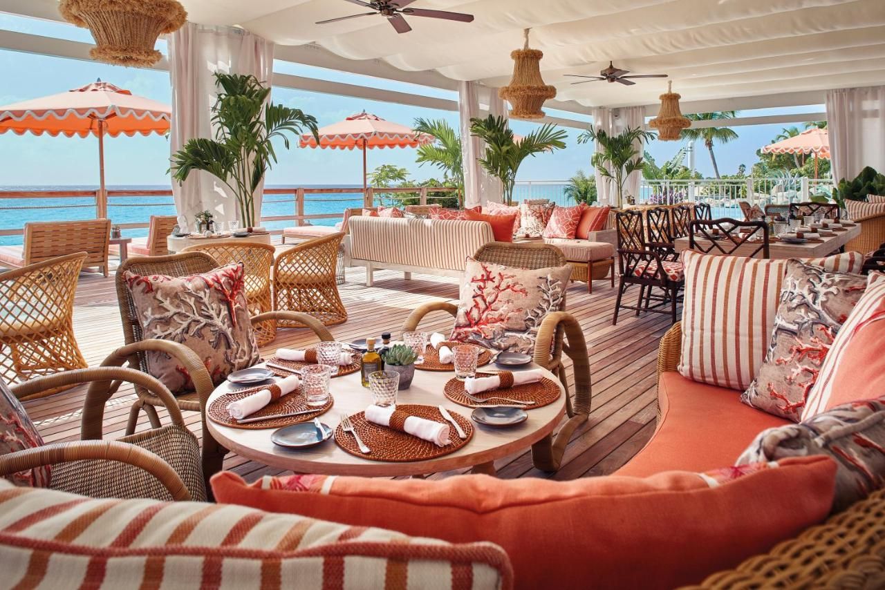 A restaurant with tables and chairs and umbrellas overlooking the ocean.