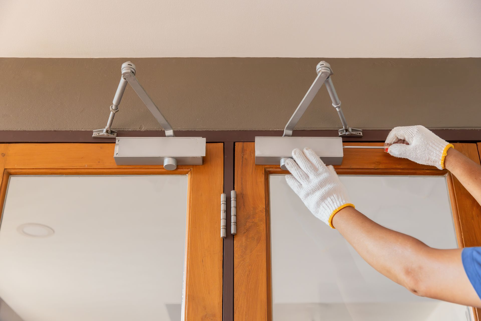 A person is installing a door closer on a wooden door.