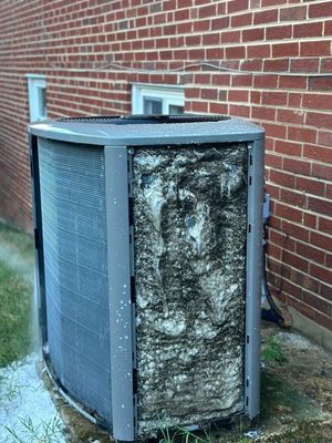 Damaged HVAC unit with exposed insulation beside a brick wall outdoors