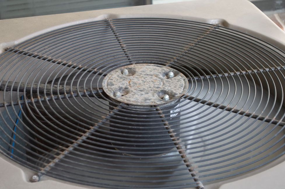 Close-up of a dusty HVAC condenser fan with metal grill and spinning blades