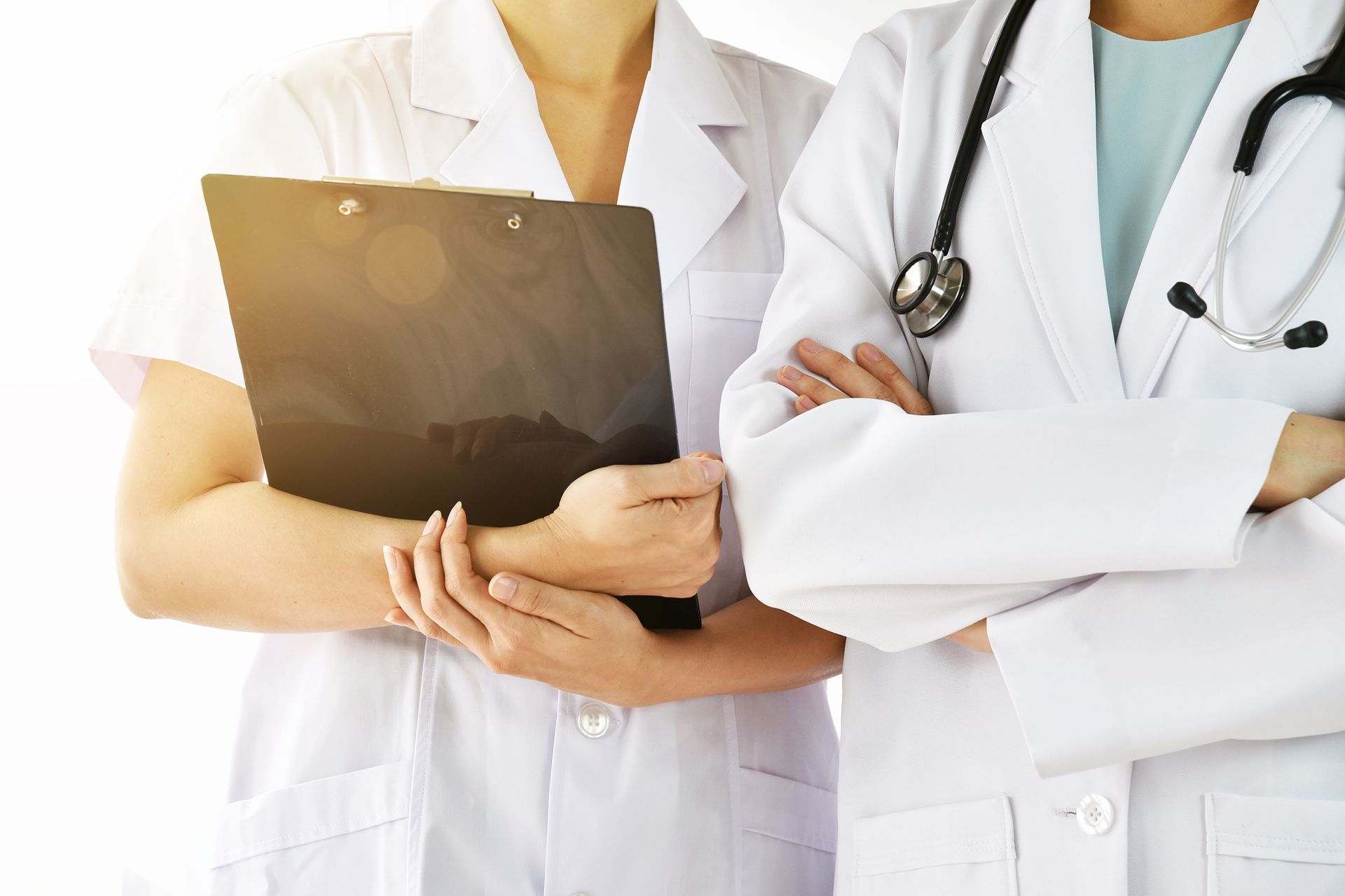 Two healthcare professionals in white lab coats, one holding a clipboard and the other with a stethoscope around their neck.