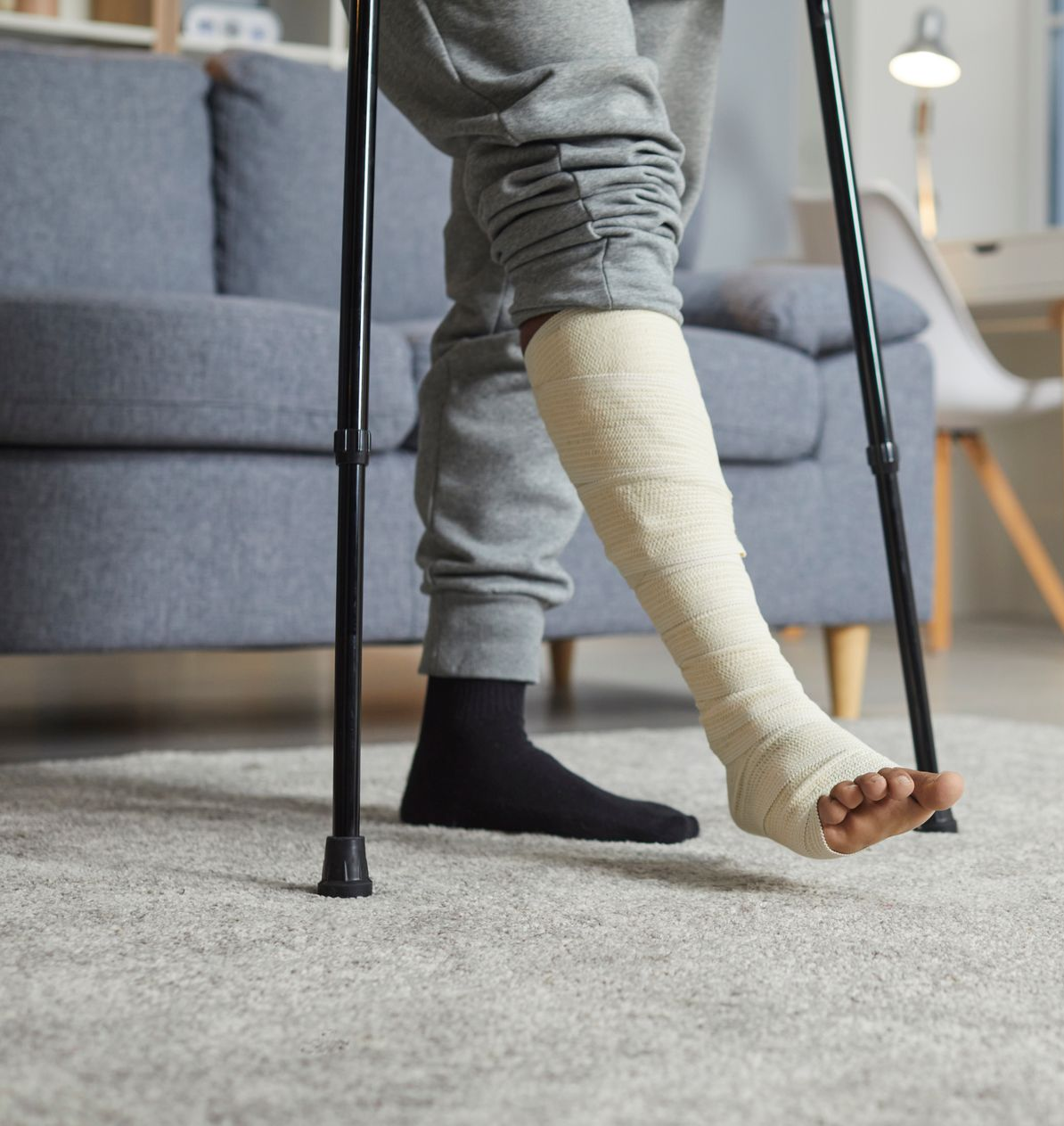 A person using crutches to stand up from a bed, wearing a protective medical boot on their lower leg.