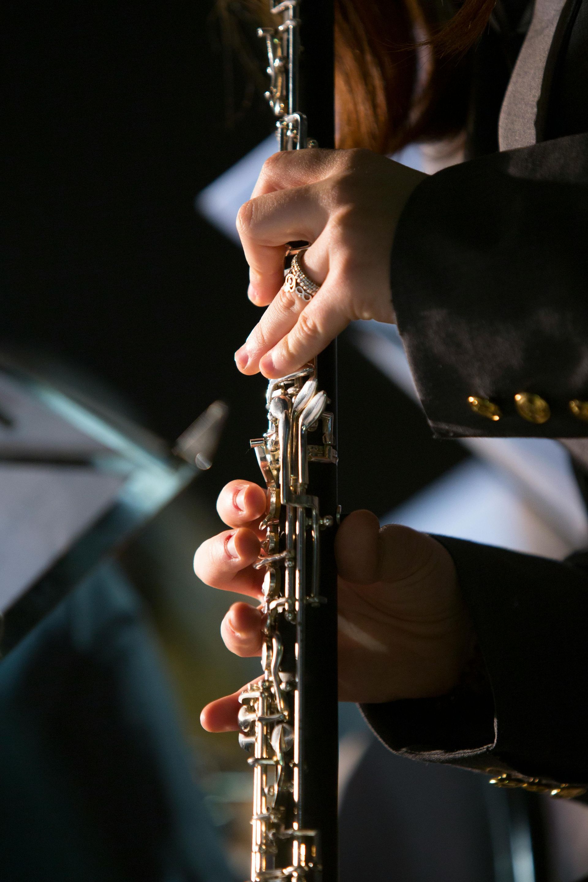 Hands playing an oboe, with buttons and silver keys.