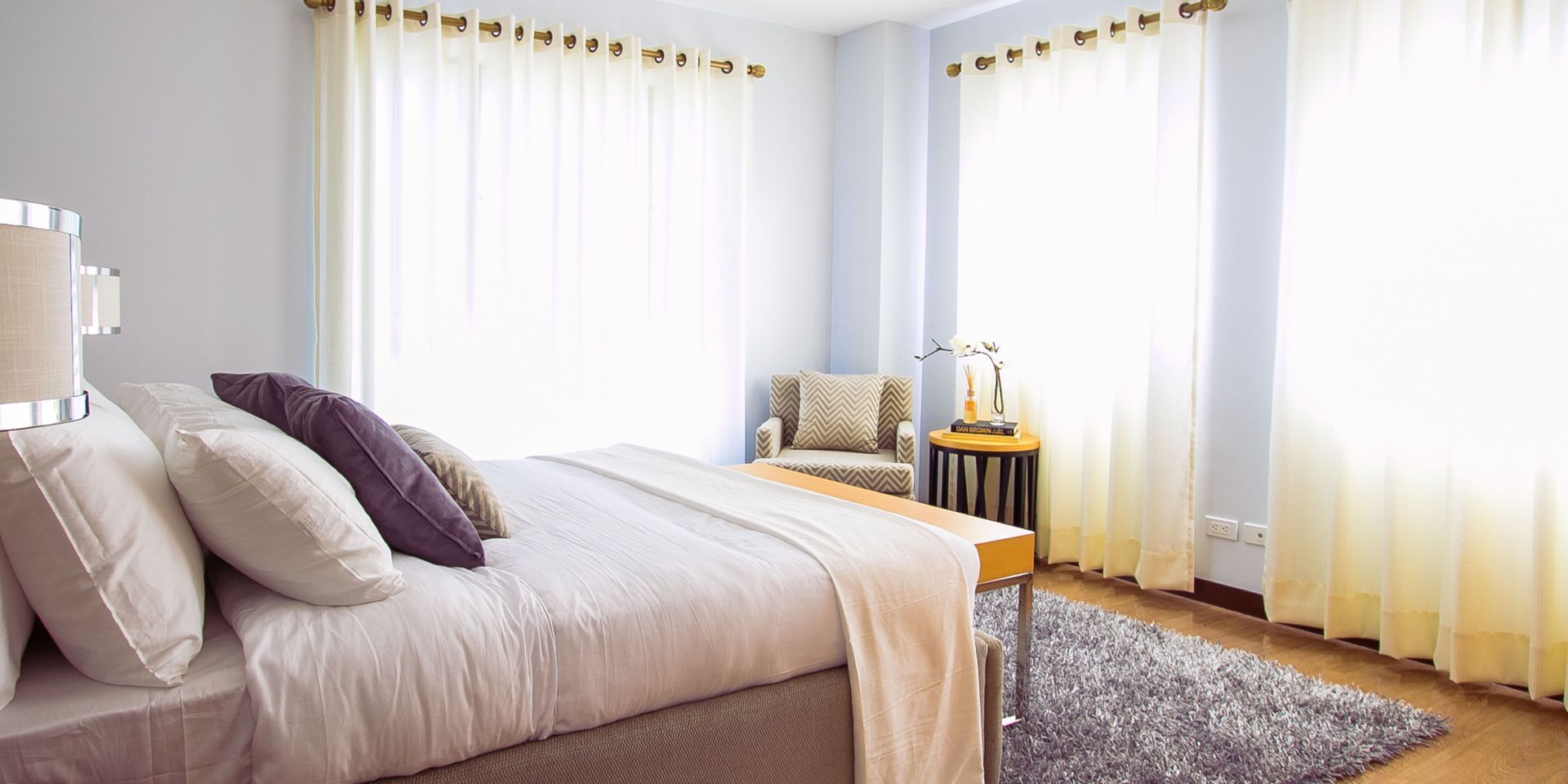 A bedroom with a bed , chair , rug and curtains.