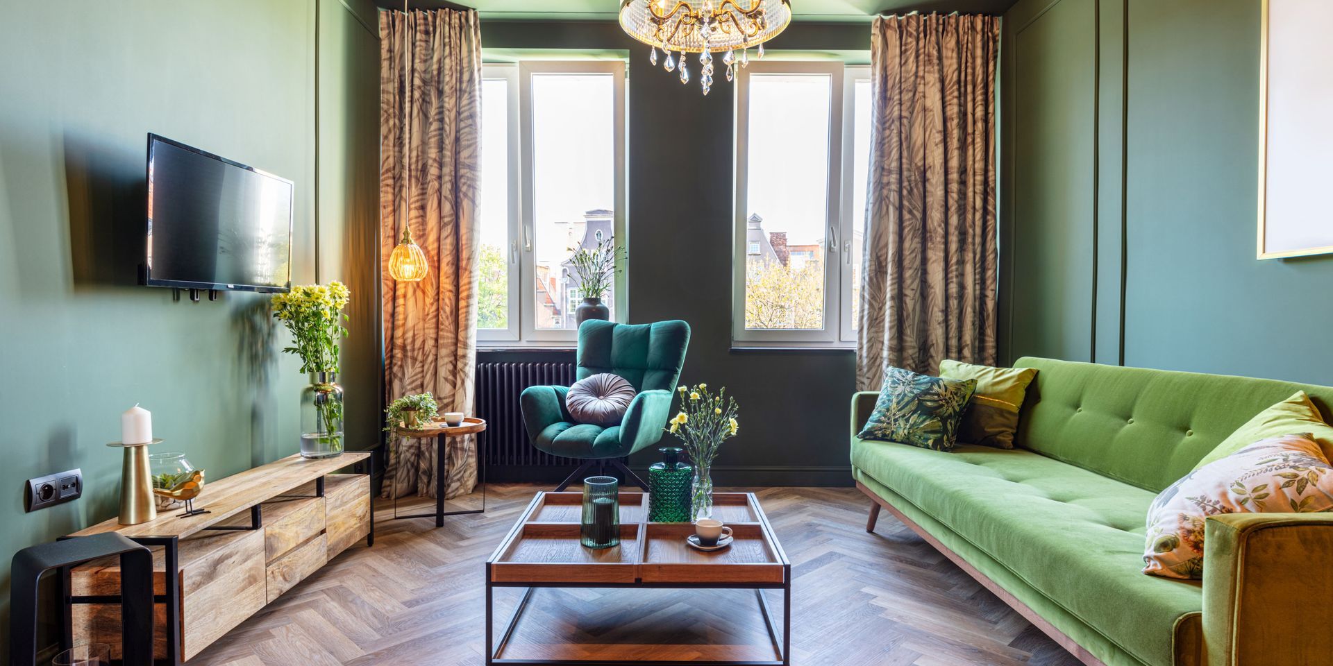 A living room with green walls , a green couch , a green chair , a coffee table and a television.