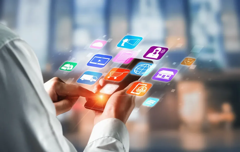 Person using a smartphone, icons floating above the screen, blurred background.