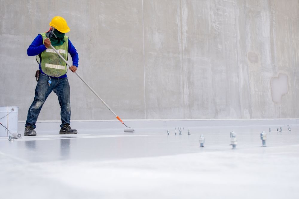 A Man Is Painting A Concrete Floor With A Roller — Eldred Waterproofing In Whitfield, QLD