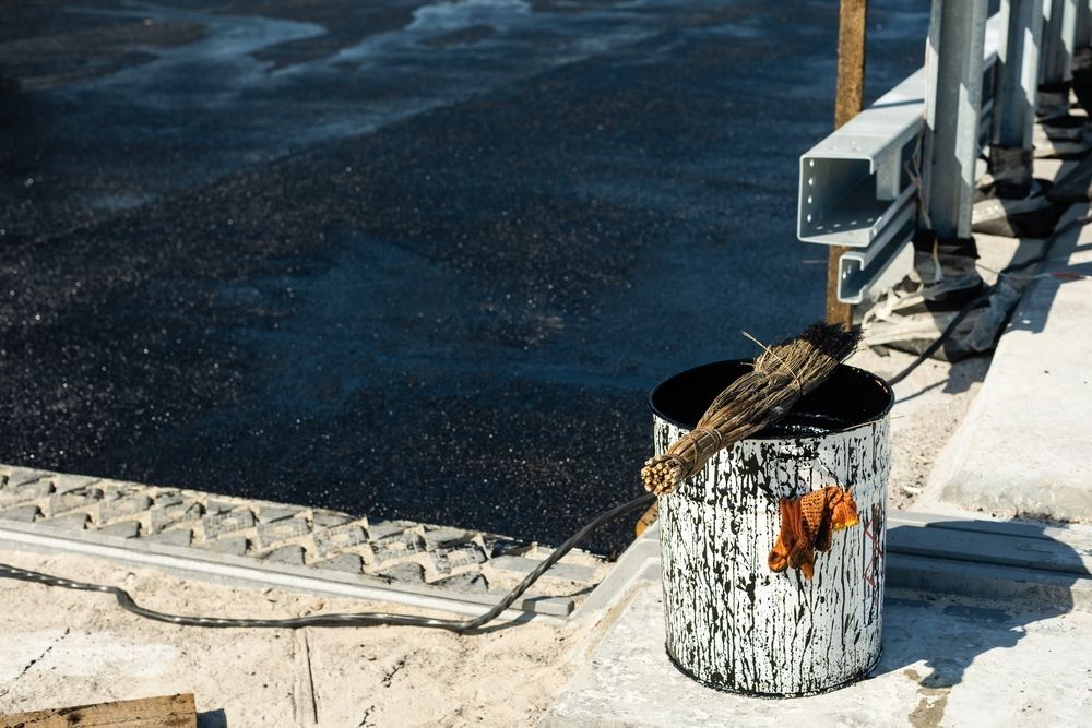 A Bucket Of Paint Is Sitting On The Side Of A Road — Eldred Waterproofing In Trinity Beach, QLD