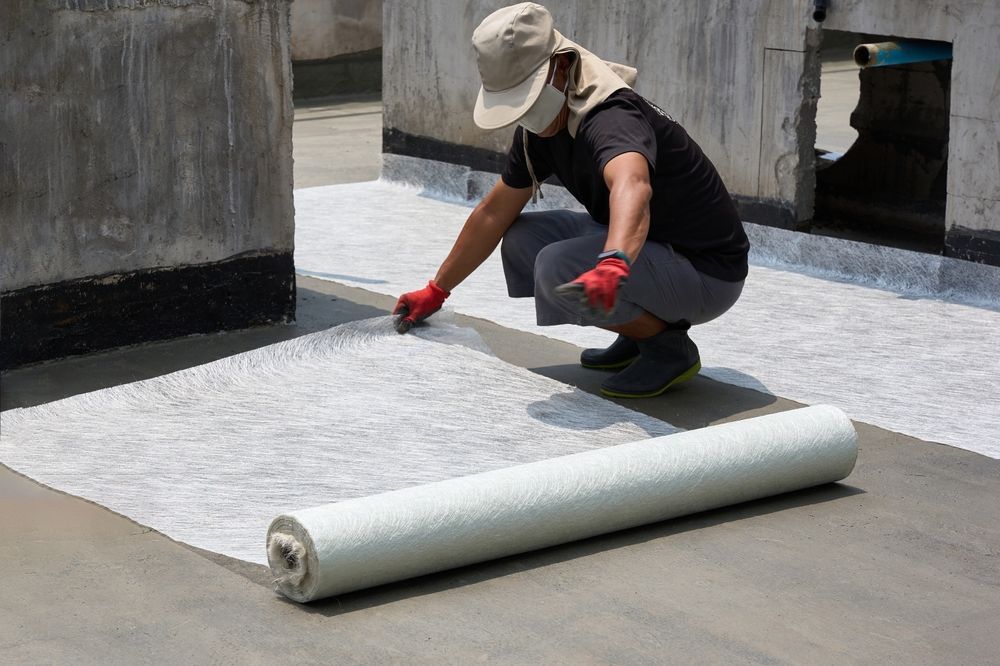 A Man Is Kneeling Down And Rolling A Roll Of Waterproofing Material On A Roof — Eldred Waterproofing In Gordonvale, QLD