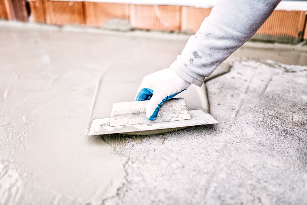 A Person Is Using A Trowel To Spread Concrete On The Ground — Eldred Waterproofing In Whitfield, QLD