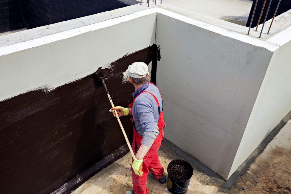A Man Is Painting A Wall With A Broom — Eldred Waterproofing In Whitfield, QLD
