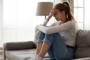 Woman sitting on a couch with head in hand, appearing stressed in a bright living room.