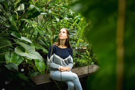 Woman sitting on a wooden bench in a lush green garden, looking upward