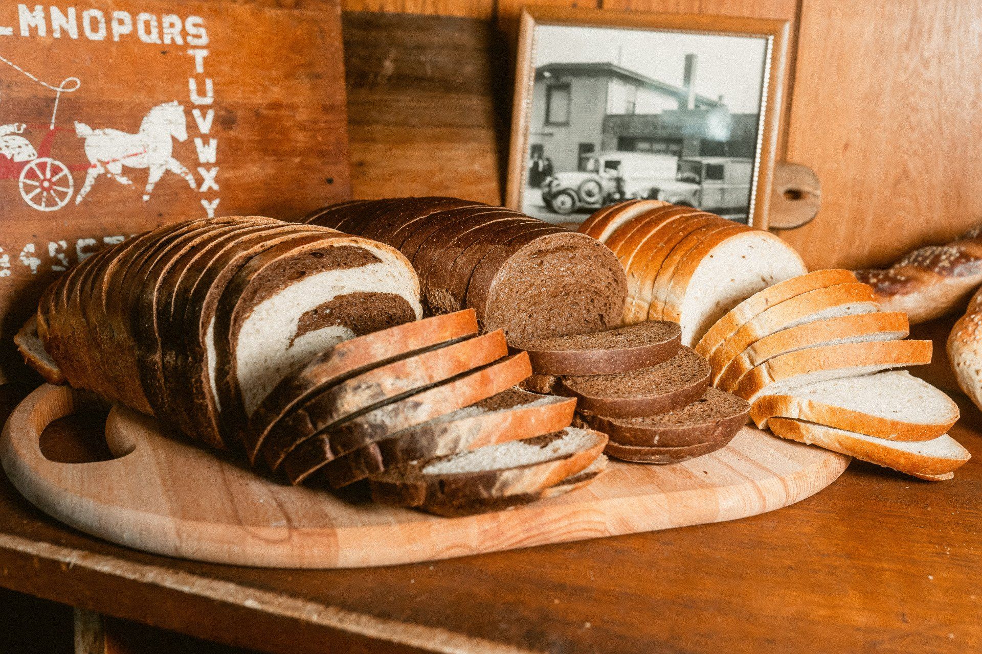 Loaves and slices of light and dark rye bread arranged on a wooden cutting board with a framed photo in the background.