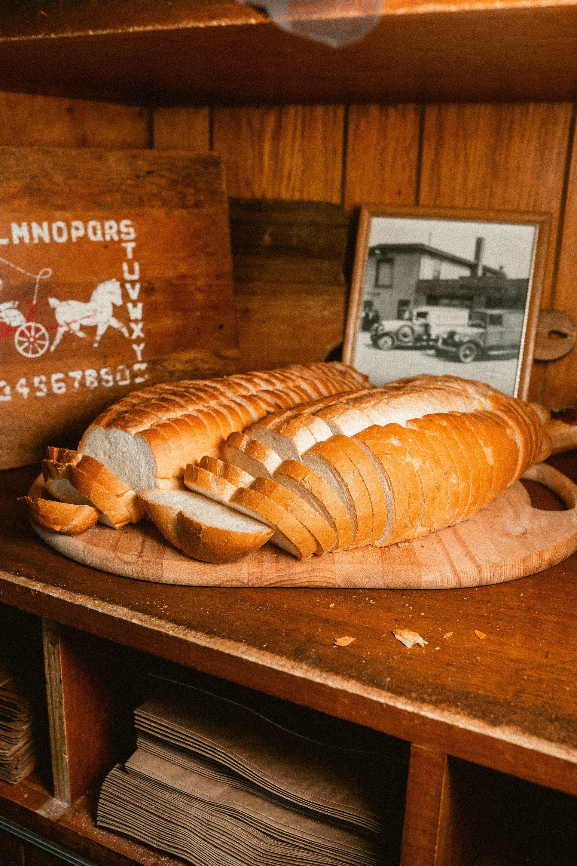 Two loaves of sliced bread rest on a wooden cutting board on a shelf next to an old photograph and a wooden alphabet board.