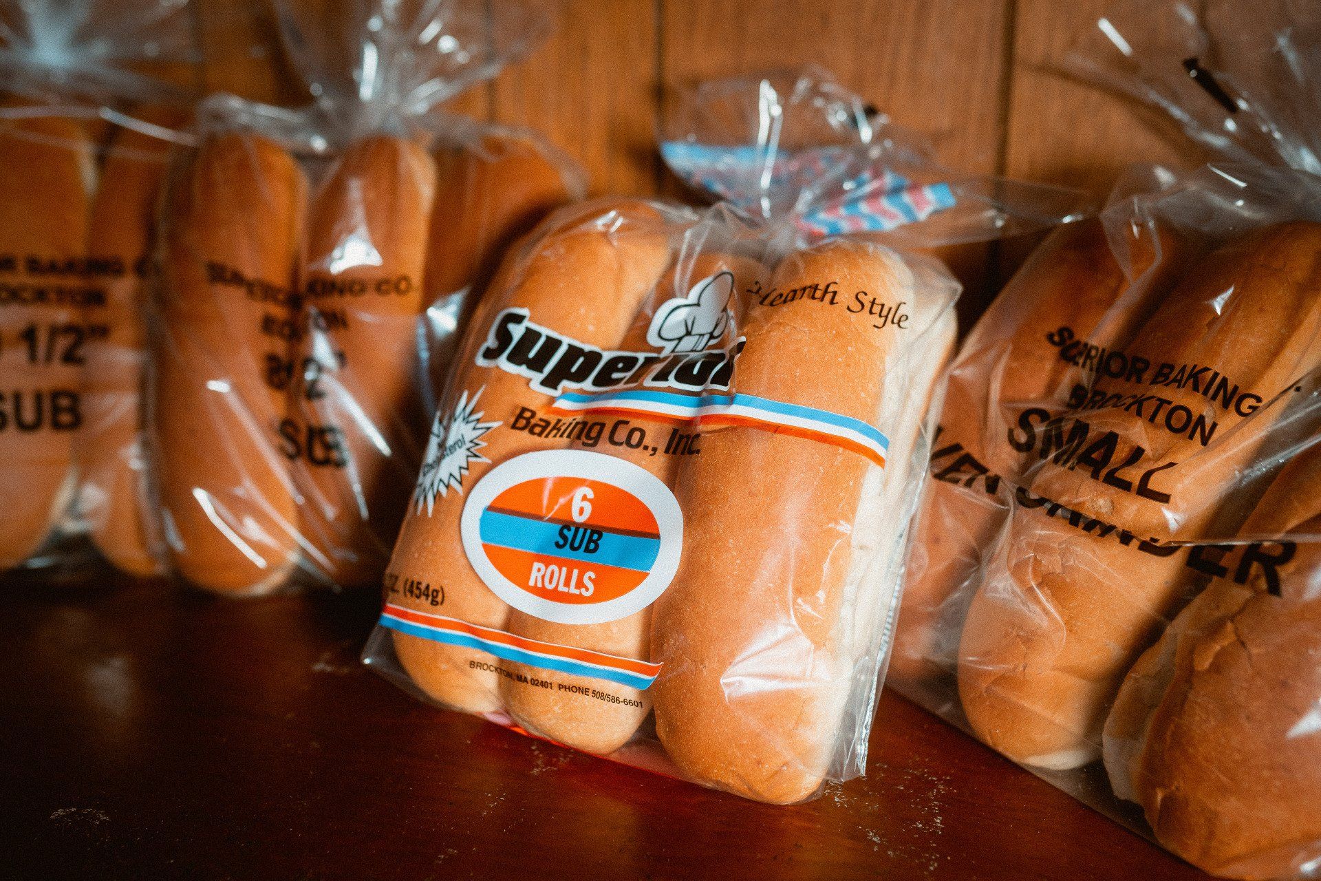Several plastic-wrapped packages of Superior Baking Co. sub and hoagie rolls arranged on a wooden surface.