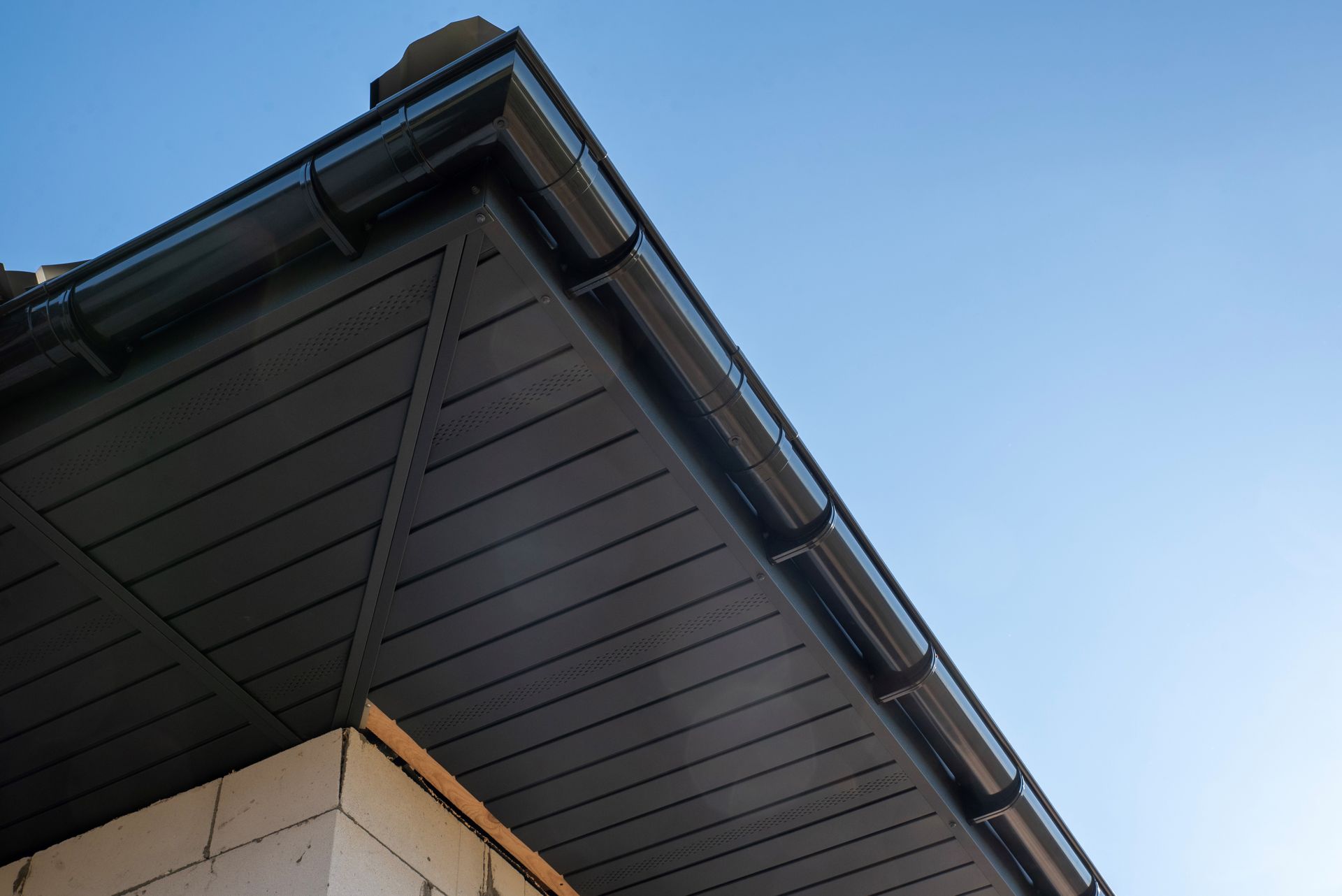 Low-angle view of a brown soffit under a roof overhang with dark gutters against a clear blue sky. Low-angle view of a brown soffit under a roof overhang with dark gutters against a clear blue sky.